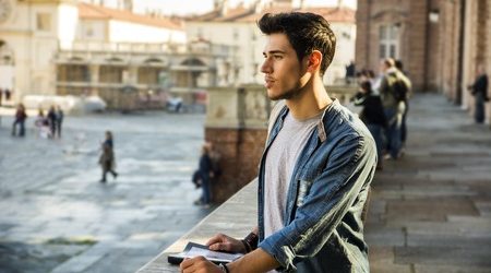 48659226 - half body shot of a thoughtful handsome young man, a tourist, holding a guide, looking away outside historic building in european city